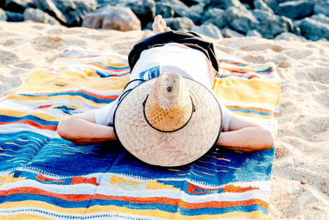 Man lounging at the beach on a mexican ethnic blanket in blue, yellow and red colours