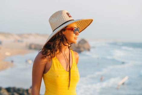 woman in yellow swimming suit and big straw hat watching the ocean
